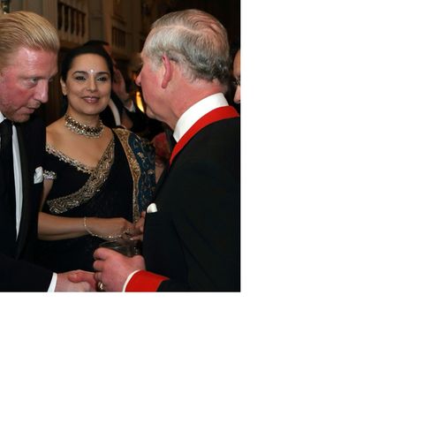 Ein Handschlag zwischen Prinz und Tennis-Star: Prinz Charles, im Dinner-Jacket mit rotem Kragen und Ärmelumschlägen, hält Small-Talk mit Boris Becker. Neben dem deutschen Tennis-Star steht seine Frau Lilly.