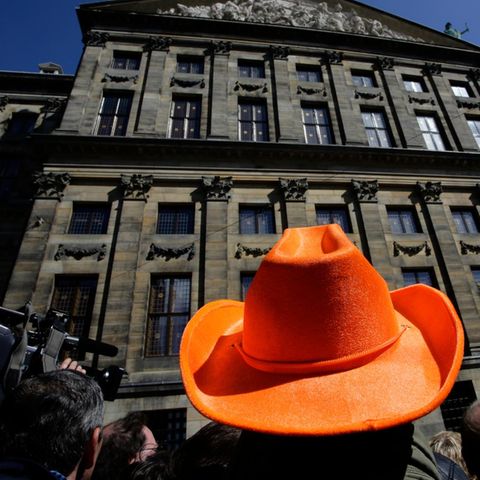 Ein Mann mit orangefarbenem Hut wartet schon am Vorabend er Abdankung vor dem königlichen Palast in Amsterdam.