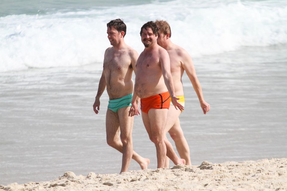 Ed Helms und Zach Galifianakis spazieren in ihren knappen, bunten Badehosen am Strand entlang.