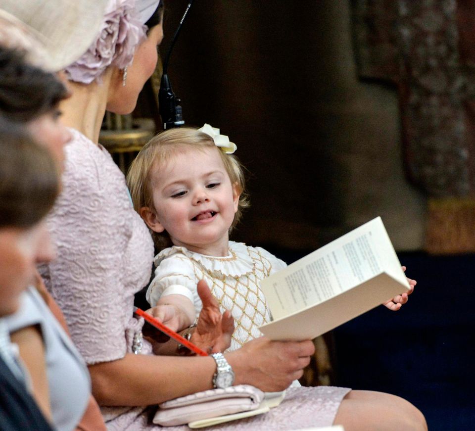 Taufe in Schweden: Estelle, auf einem eigenen Ministuhl, hat schon das Gottesdienstprogramm angeschaut und möchte nun ihr Bilderbuch. Estelle, auf einem eigenen Ministuhl, hat schon das Gottesdienstprogramm angeschaut und möchte nun ihr Bilderbuch.