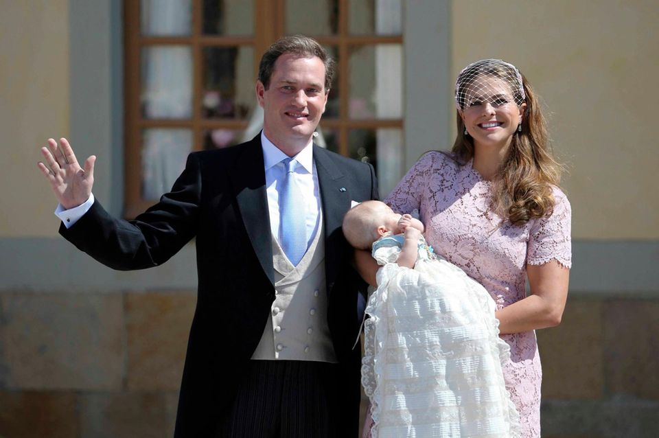 Prinzen-Taufe in Schweden: Prinzessin Leonore schlummert auf dem Arm ihrer Mutter in dem königlichen Taufkleid. Die Eltern zeigen sich mit dem Täufling den vielen Schaulustigen, die bei strahlendem Sonnenschein gewartet haben. Prinzessin Madeleine trägt ein Kleid in zartem rosé mit Spitze aus dem Hause "Valentino".
