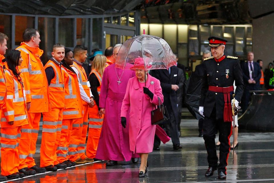 Die Queen kommt in einem pinken Mantel nach Birmingham, dessen leuchtende Farbe besonders stark auffällt, als sie von den Metro-Mitarbeitern umgeben ist.