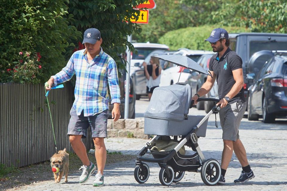 Prinz Carl Philip schiebt Baby Alexander, während ein Begleiter Border Terrier Siri an der Leine führt.