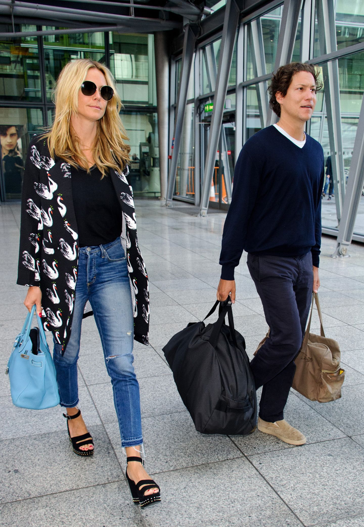 Wie praktisch, wenn der Freund ein Gentleman ist und die schweren Reisetaschen schleppt. So kann sich Heidi Klum neben ihrem Vito mit dem stylischen Schwanen-Mantel und den engen Jeans in voller Pracht zeigen.