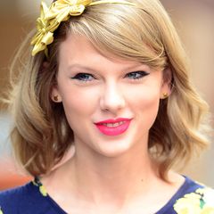 Zwei goldgelbe Seidenblüten auf dem Haarreifen unterstreichen Taylor Swifts frühlingshaften Look.