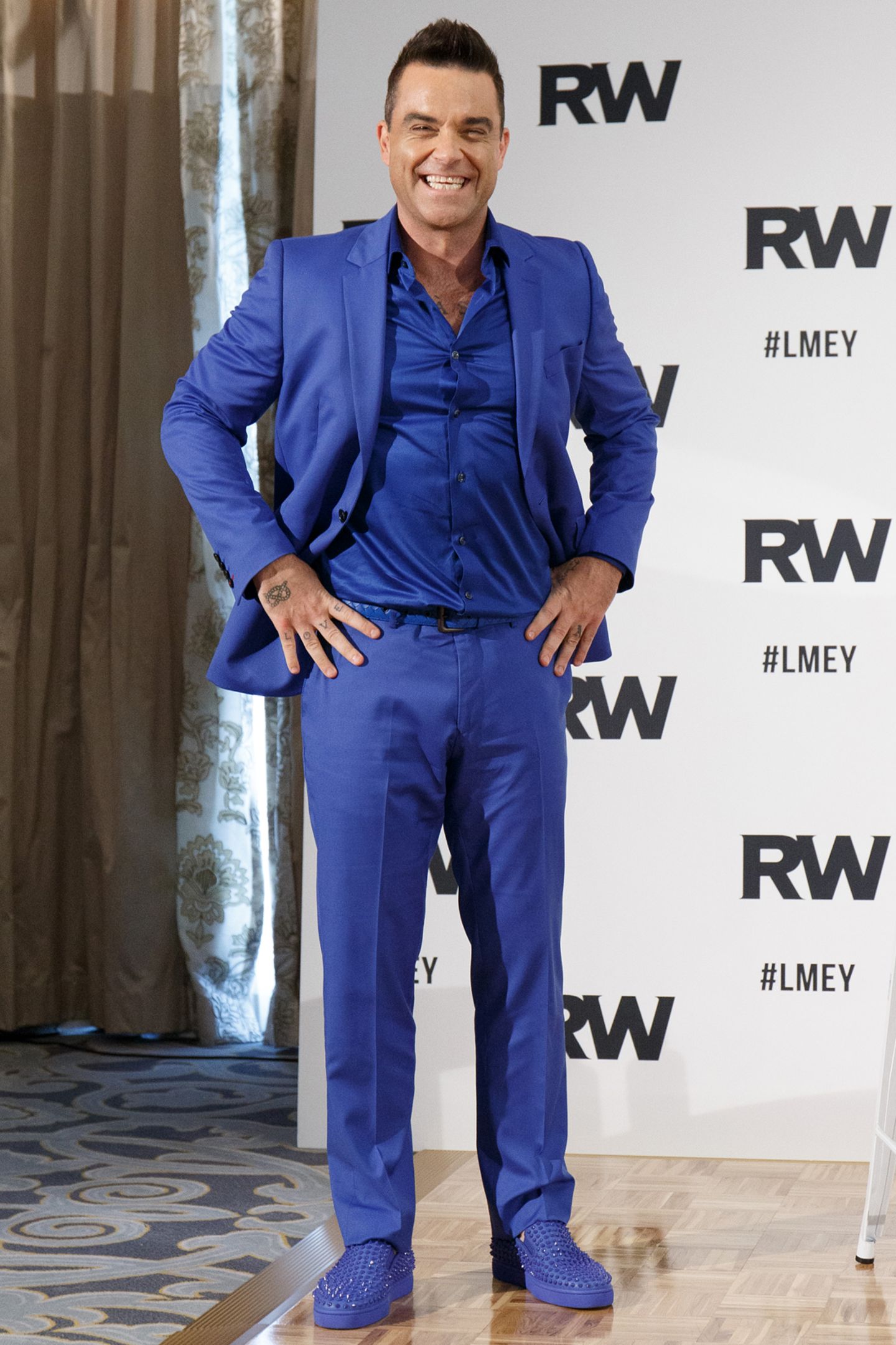 Robbie Williams macht blau: Im kobaltblauen Komplettlook promotet der smarte Entertainer seine anstehende Tournee. Seine knalligen Slipper sind zusätzlich sogar noch mit funkelnden Nieten besetzt.