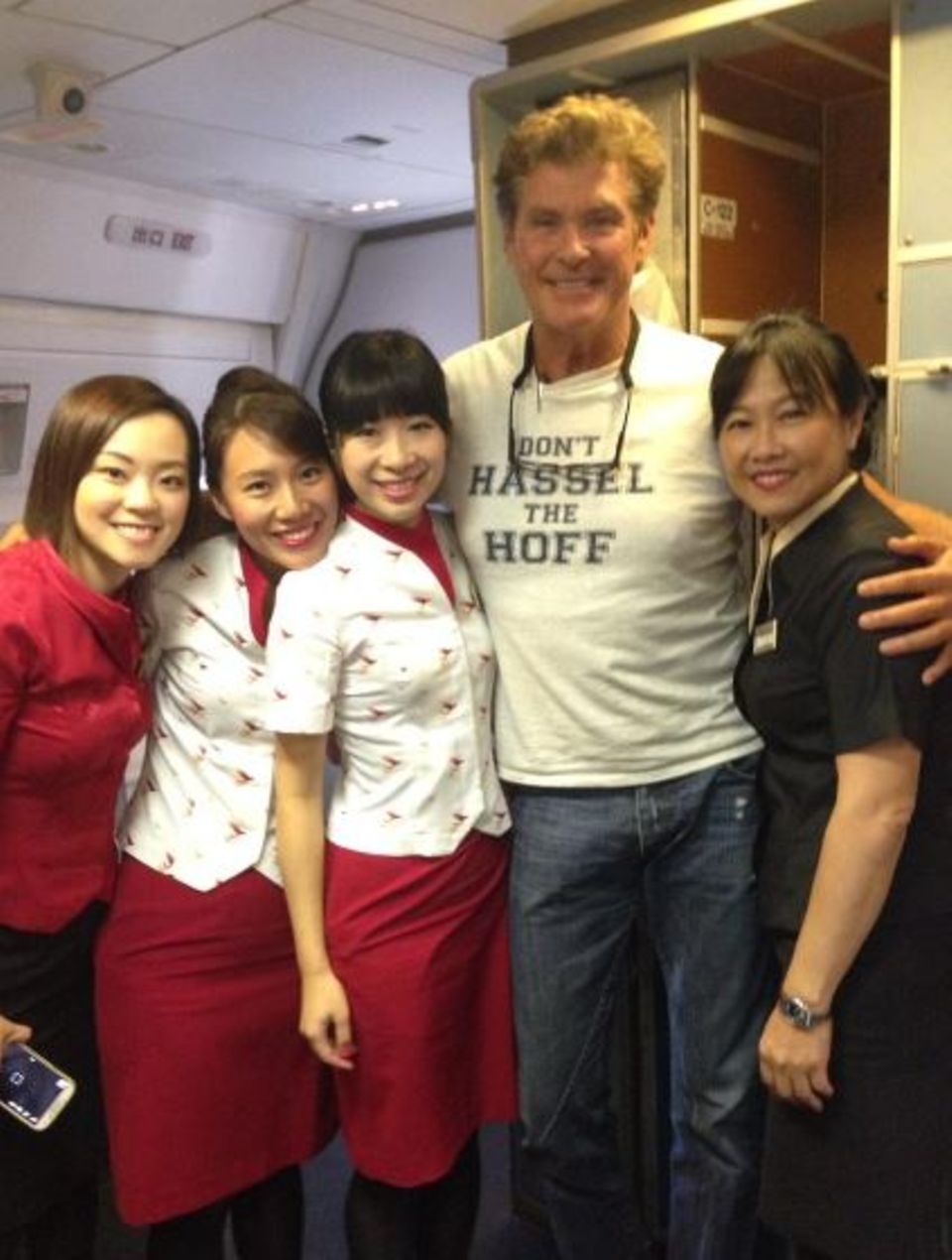 David Hasselhoff lächelt mit den Stewardessen auf seinem Flug nach Bali in die Kamera und verkündet auf seinem Shirt "Don't Hassell The Hoff". David Hasselhoff lächelt mit den Stewardessen auf seinem Flug nach Bali in die Kamera und verkündet auf seinem Shirt "Don't Hassell The Hoff".