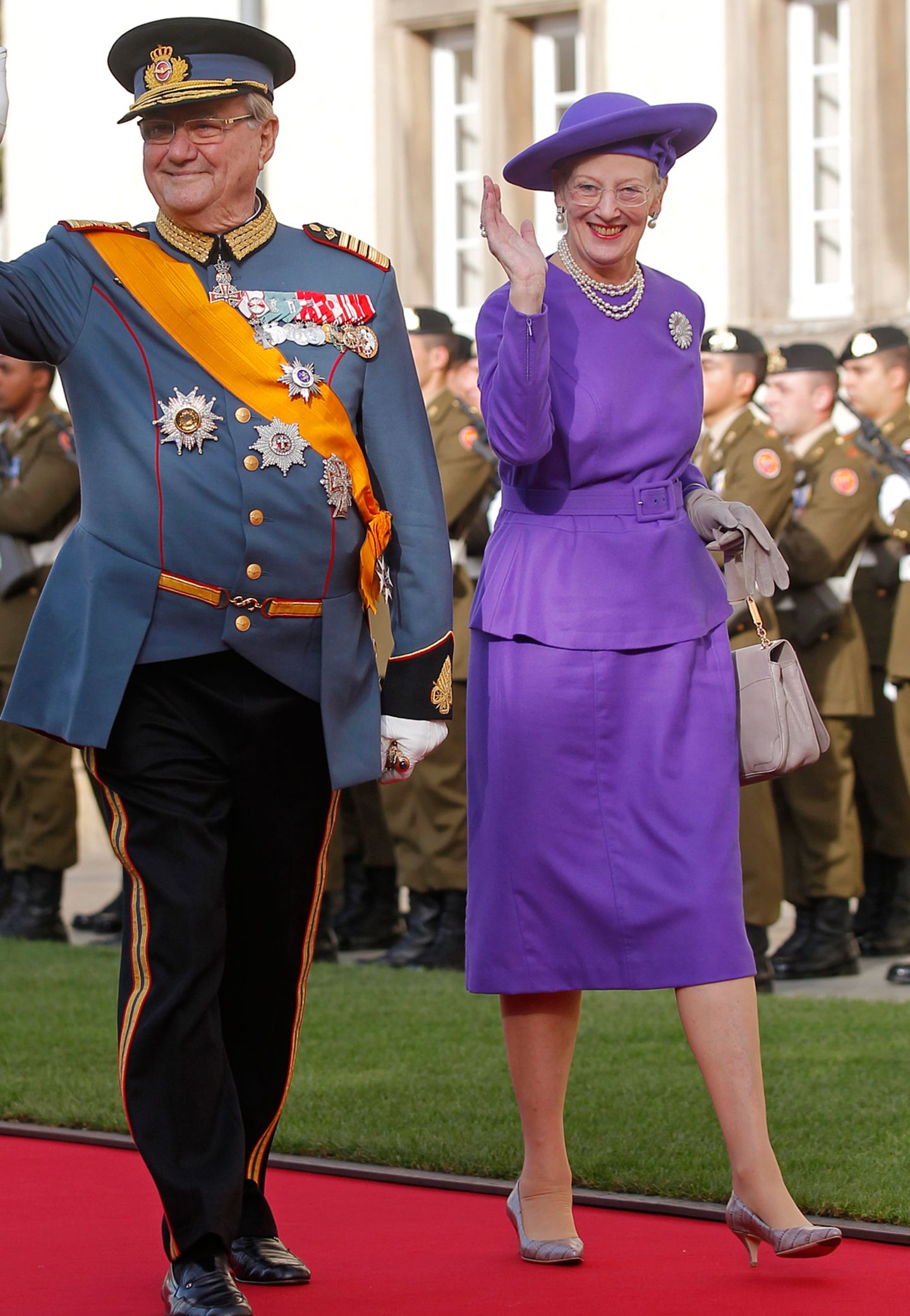 Den Hochzeitsgästen des Luxemburger Großherzogpaars winkt Königin Margrethe in einem leuchtend lilafarbenen Ensemble zu.