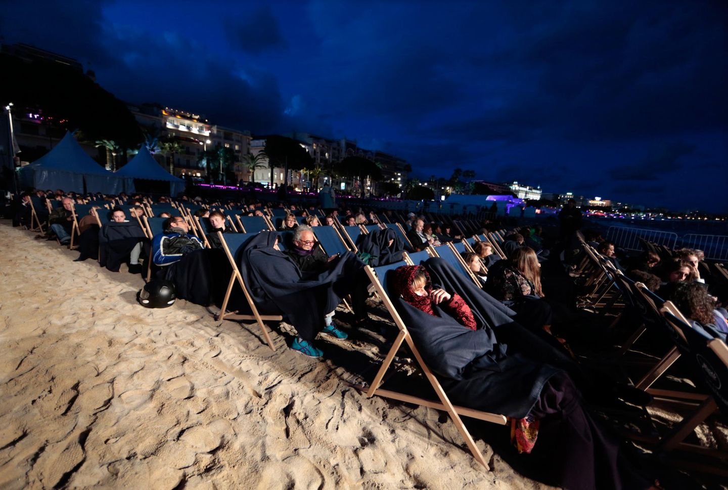 Dick eingepackt mummeln sich Festival-Zuschauer am Strand in ihre Liegestühle.