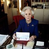 Prinzessin Lilian von Schweden, die Tante von König Carl Gustaf, verfasst an ihrem Schreibtisch sitzend eine Weihnachtskarte. Zum Lesen der Unterlagen oder des Adressbuches, die vor ihr liegen, braucht sie offenbar eine Lupe. Gleich zwei befinden sich in der Nähe. Und falls sich die damals 81-jährige Prinzessin ausruhen möchte, muss sie gar nicht weit gehen. Auf dem Bild aus dem Jahr 1996 ist im Hintergrund ein Bett zu erkennen.