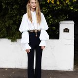 Weiße Bluse mit weiten Ärmeln im viktorianischen Stil, dazu schmale schwarze Schlaghose, lange Goldkette und metallverzierter Gürtel, alles von Alexander McQueen