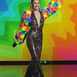 Miley In The Sky With Diamonds?! Welche fragwürdigen Substanzen der Designer dieses Outfits vor dem kreativen Prozess konsumierte, ist leider nicht überliefert. Irgendwie erinnert der Flower-Power-Overall-Albtraum aber an die feuchtfröhlichen Schlager-Partys, die wir Deutschen so schrecklich gerne feiern.