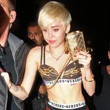 Was, ja was hat sich Miley Cyrus bei diesem Outfit gedacht? Liz-Hurley-Gedächtnis-Nadeln an der Strumpfhose, prollige Unterwäsche von Versace Versus, Holzfällerhemd und Tanzkurs-Treter ergeben zusammen ein Outfit, ähnlich schrecklich wie der Gesichtsausdruck ihres Begleiters.