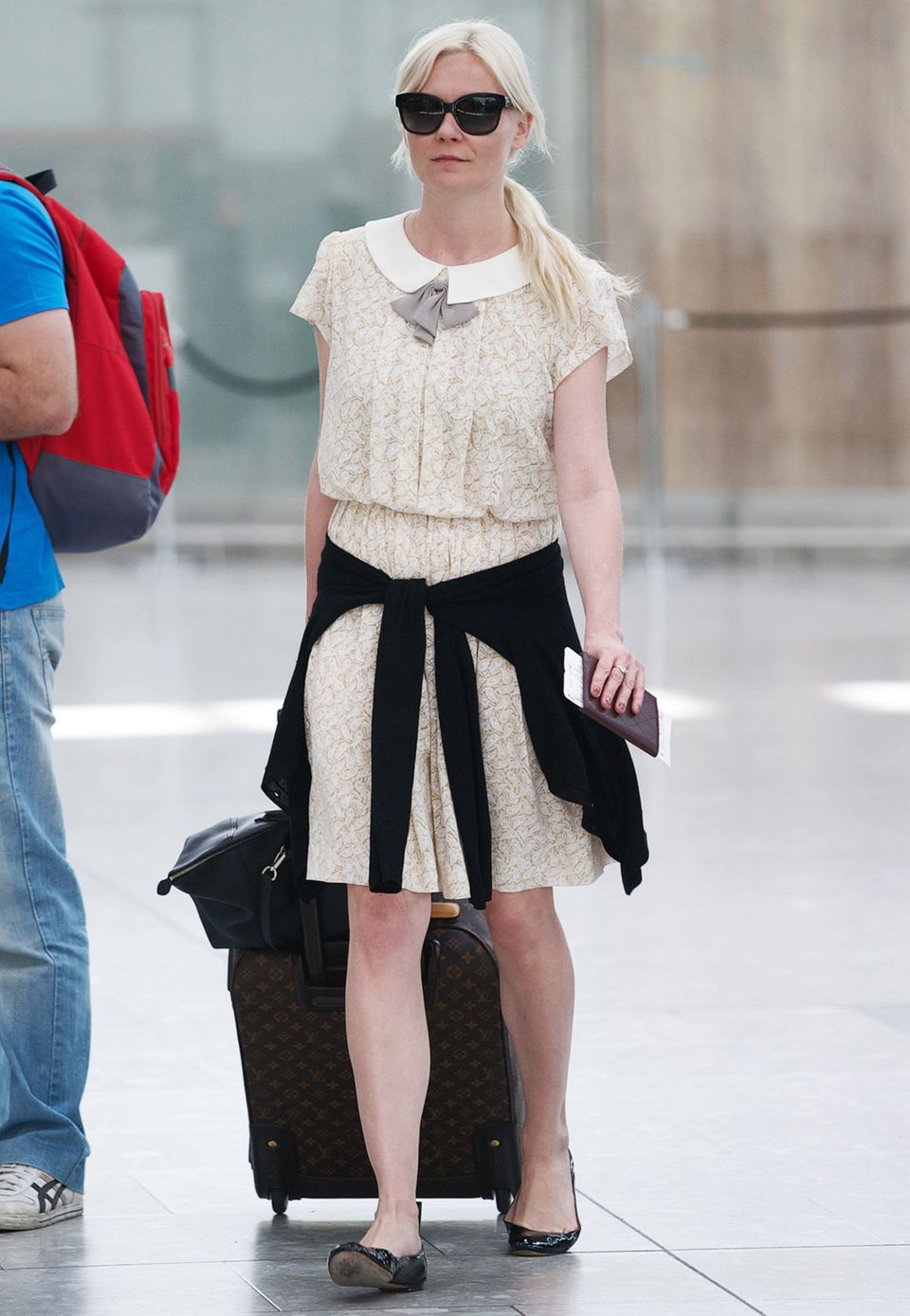 Kirsten Dunst ist auch auf Reisen eine echte Lady: Das süße Sommerkleid mit Kragen und kleiner Schleife kombiniert sie zu flachen Lackleder-Ballerinas und einem geräumigen, schwarzen Shopper.