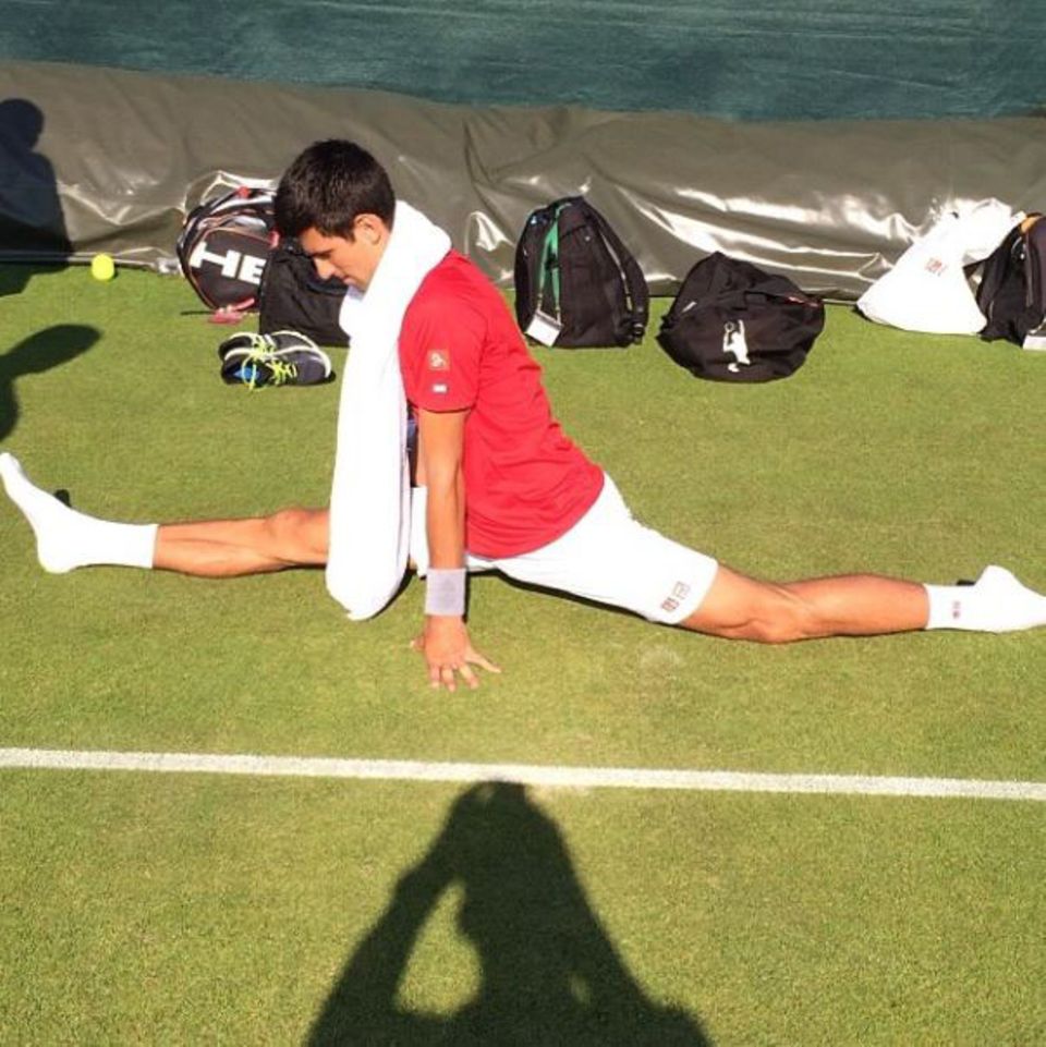 Novak Djokovic dehnt sich ausgiebig nach dem Training. Boris Becker hält das auf Kamera fest.