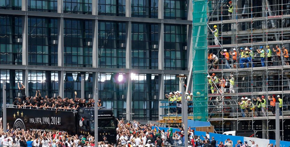 Hunderttausende säumen den Weg vom Flughafen zur Fanmeile am Brandenburger Tor und jubeln den neuen Fußballweltmeistern zu. Selbst die Bauearbeiter lassen für Neuer, Schweinsteiger, Özil und Co. alles stehen und liegen. Wegen der Fanmassen musste der WM-Truck immer wieder stoppen.