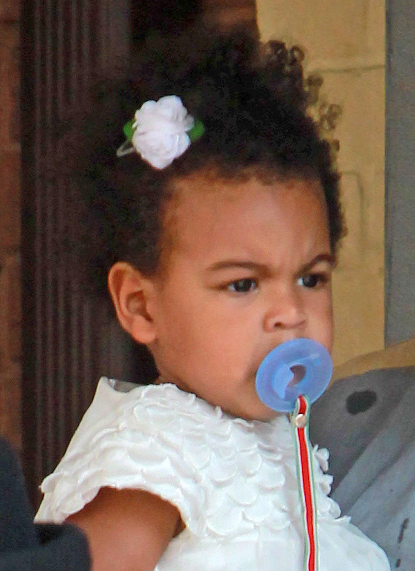 Passend zum Kleid haben Mama Beyoncé und Papa Jay-Z Blue Ivys Haar mit einer weißen Blume geschmückt. Besonders erfreut scheint die Kleine darüber aber nicht zu sein.