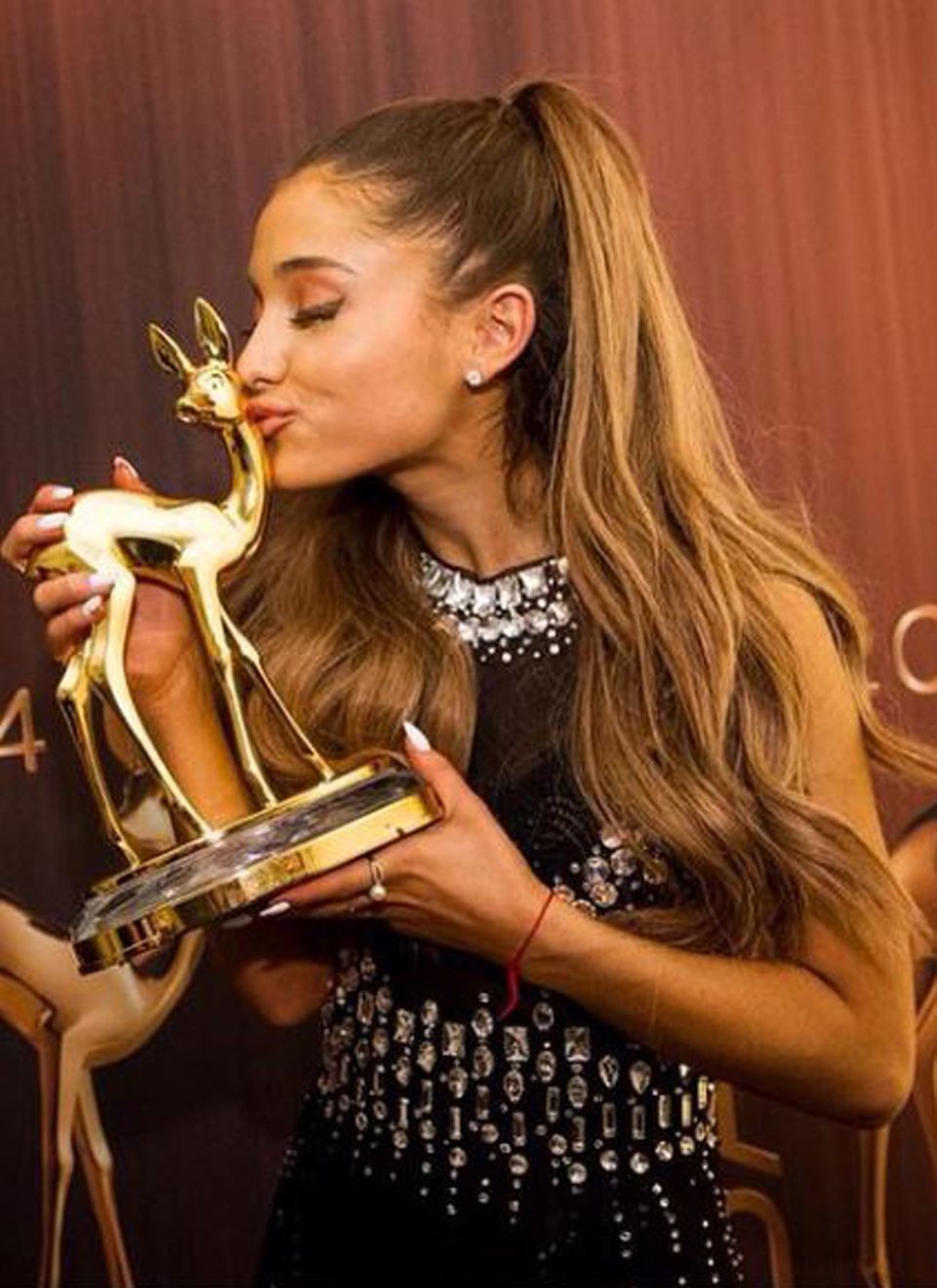 Was für eine Freude: Sängerin Ariana Grande küsst ihren Bambi. Der expressive Eyeliner-Look passt toll zum streng hochgekämmten Pferdeschwanz. Den weißen Nagellack hat sie auf die Schmuckstein am Kleid abgestimmt.