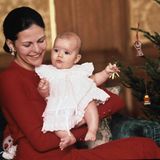 1977  Prinzessin Victoria ist knapp fünf Monate alt, als sie zum ersten Mal Weihnachten erlebt. Im weißen Kleidchen und bei ihrer Mutter Silvia auf dem Arm guckt sie ganz erstaunt, als das erste Weihnachtsbild von ihr entsteht.