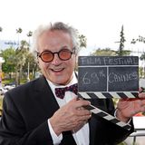 Regisseur George Miller strahlt, mit einer Filmklappe in der Hand, in die Kamera. Er leitet die diesjährige Jury in Cannes.