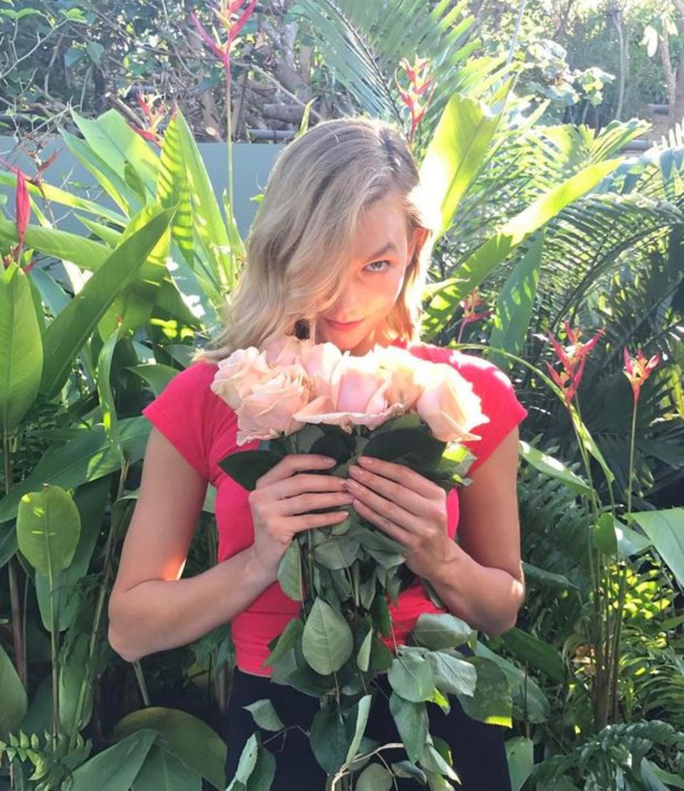 Model Karlie Kloss schnuppert an einem Strauß Rosen.