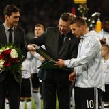 DFB-Präsident Reinhard Grindel überreicht Lukas Podolski vor der Partie gegen England ein Geschenk.