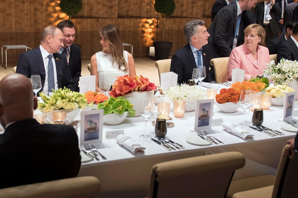Melania Trump bei "G20": Ein Dolmetscher hilft bei der Verständigung zwischen US-First-Lady und Kreml-Chef. Angela Merkel schaut interessiert zu. Melania Trump und Wladimir Putin bei einem Dinner in der Elbphilharmonie im Rahmen des "G20"-Gipfels in Hamburg