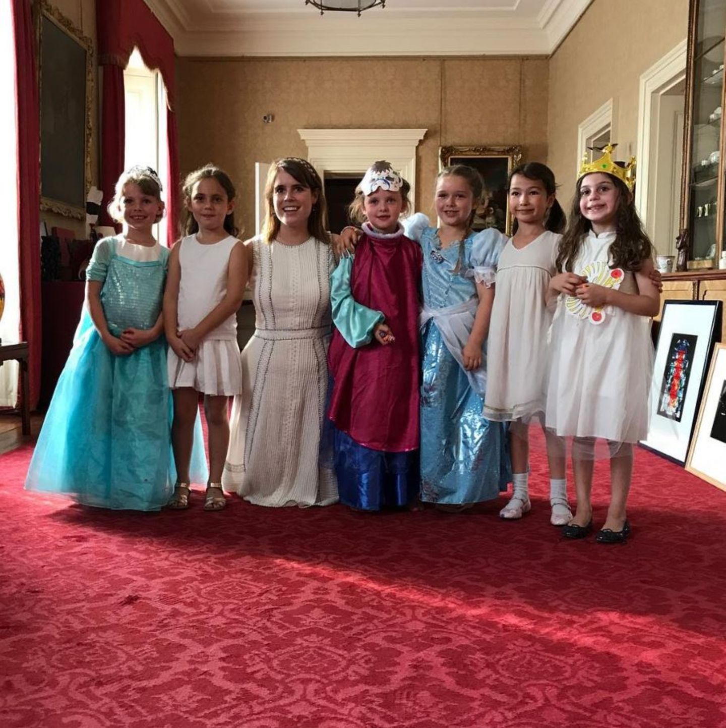 Sechs verkleidete Prinzessinnen und eine echte: Harper und ihre Freundinnen - die alle als Prinzessinnen verkleidet sind - treffen die waschechte Prinzessin Eugenie von York während der Feierlichkeiten im Kensington Palast. Stolz lächelt die Mädchen-Truppe in die Kamera. 