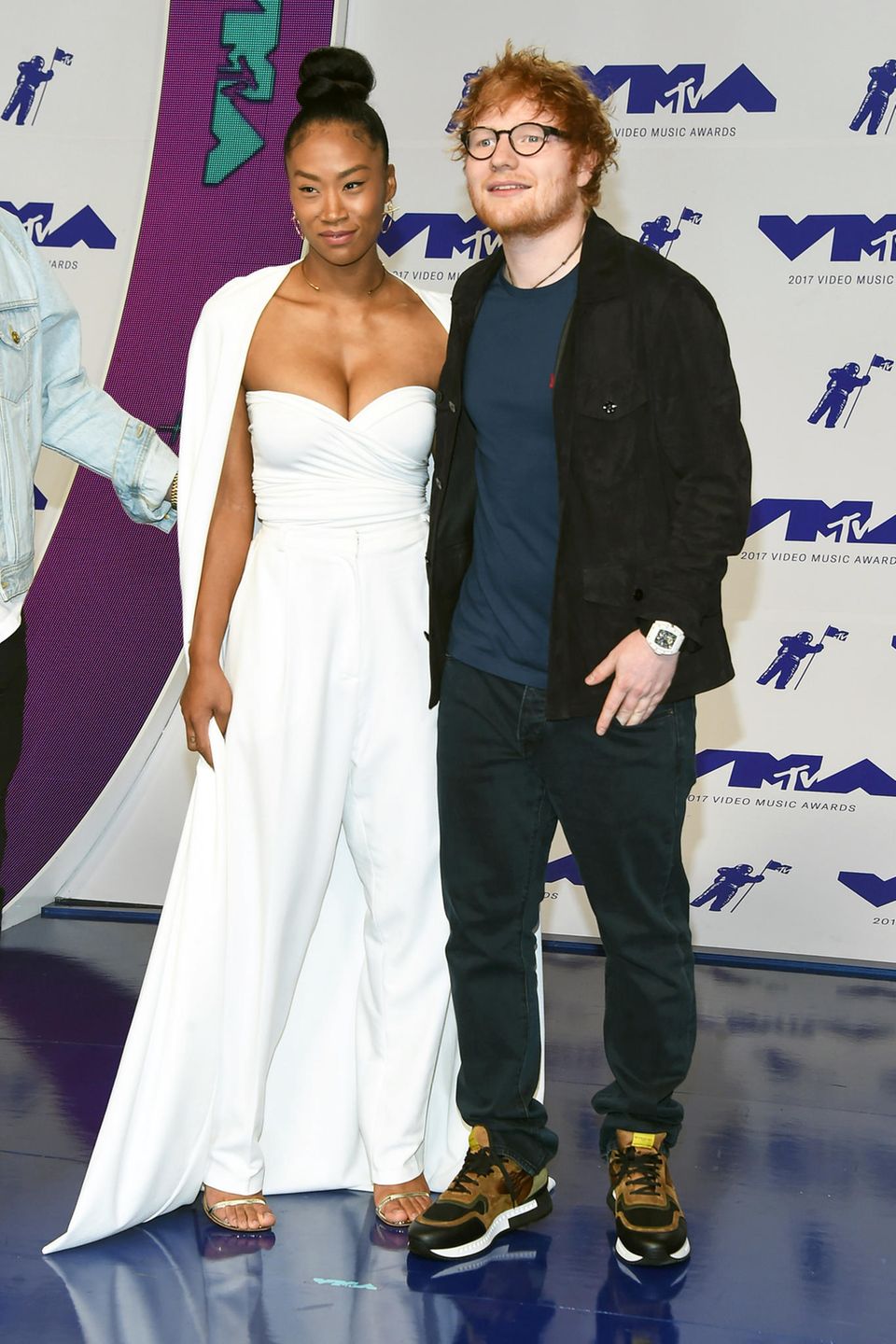 Ed Sheeran zeigt sich wie üblich im Schlabber-Look, seine Freundin Jennie Pegouskie hingegen bezaubert im weißen Glamour-Jumpsuit mit Cape. 