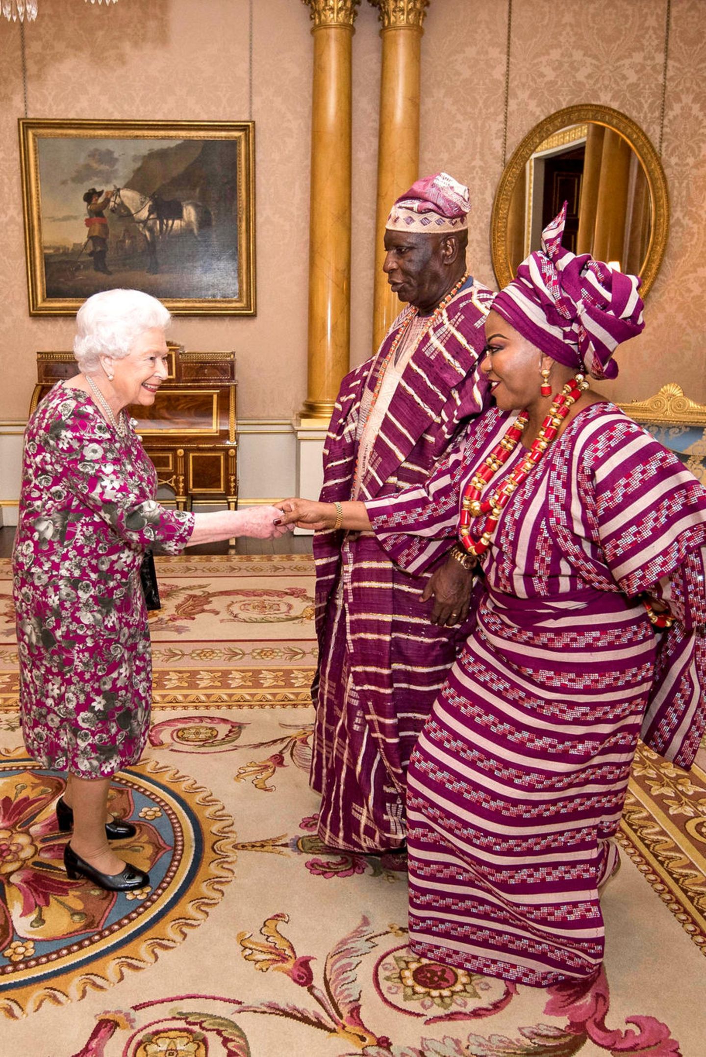 6. Dezember 2017  Queen Elizabeth empfängt George Adesola Oguntade aus Nigeria mit seiner Frau zu einer Privataudienz im Buckingham Palace. Dabei sind alle Augen auf die traditionelle Kleidung der Gäste gerichtet, die perfekt mit dem Kleid der Queen harmoniert. 