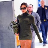 Am JFK-Airport in New York flaniert Victoria in einem olivfarbenen Rollkragenpullover und orangefarbenem Plissee-Rock zu ihrem Gate. 