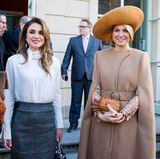 Königin Máxima trägt unter dem Mantel ein langärmeliges Spitzenkleid von Claes Iversen, das nur dank der offenen Ärmel rausblitzt. Königin Rania hingegen hat ihren Mantel abgelegt und zeigt, dass sie darunter einen dunkelgrauen Bleistiftrock und eine weiße durchsichtige Bluse trägt. 