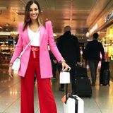 Was für ein cooler Look! Jana Ina Zarella setzt auf absolutes Colour-Blocking mit einer roten Schlaghose in Kombination mit einem pinkfarbenen Longblazer und zieht damit alle Blicke am Flughafen auf sich.