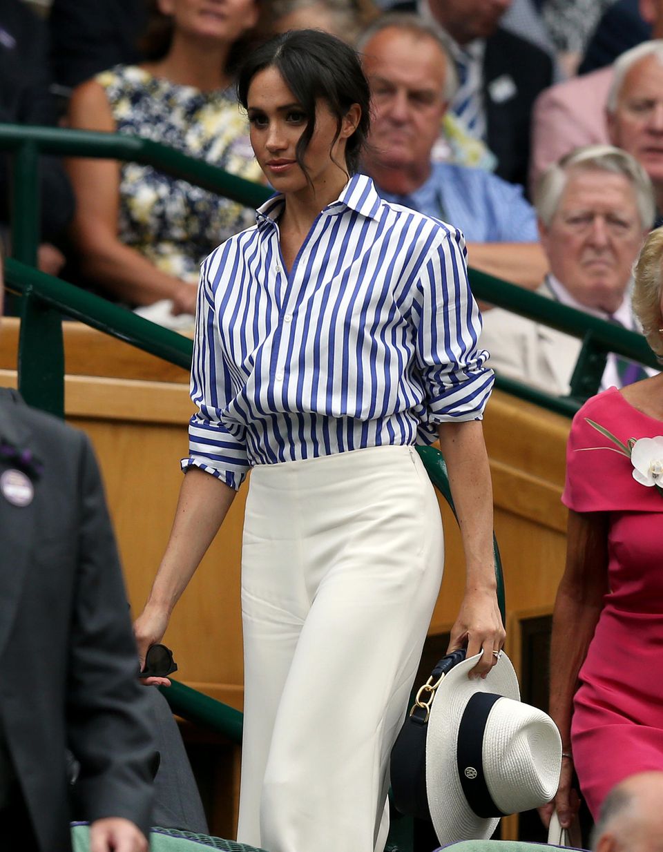 Herzogin Meghan: In 2018 kommt Herzogin Meghan in einem tollen Outfit nach Wimbledon. Zur gestreiften Bluse kombiniert sie eine weite Hose und einen sommerlichen Strohhut. Diesen behält sie aber - wie auch ihre Tasche von Altuzarra - in der Hand. In der Hand hält sie eine dunkelblaue Handtasche von Altuzzara und einen hellen Strohhut, den sie jedoch nicht aufzusetzen scheint. Sie hält ihn die ganze Zeit in der Hand.