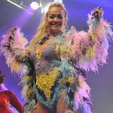 Egal ob beim Streetstyle oder beim Bühnenlook: Sängerin Rita Ora mag es gerne flippig! Beim Manchester Pride Festival überrascht sie ihre Fans mit einem ausgeflippten, bunten Feder-Umhang, ebenfalls bunten Häkel-Body, einer sexy Netzstrumpfhose und gelben Plateau-Schuhen von Naked Wolfe. Dieses Outfit eignet sich einfach wunderbar zum ...