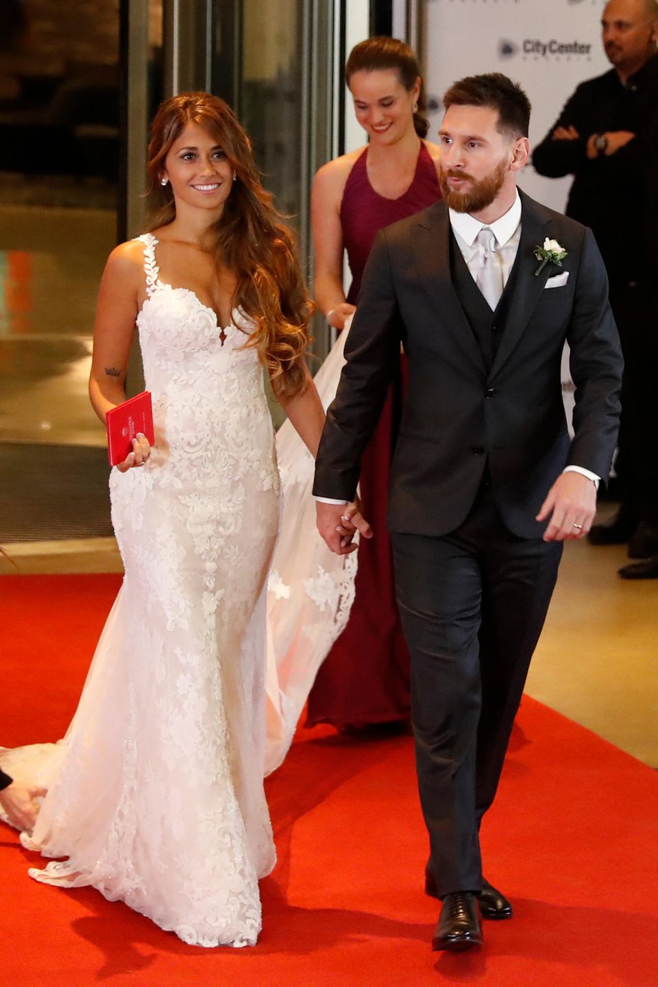 Lionel Messi heiratet seine Antonella: Sie trägt ein enges weißes Kleid mit Spitzenüberzug und dünnen Trägern. Besondere Hingucker sind der spitze Ausschnitt und das rote Familienstammbuch, das einen farblichen Akzent bildet. 
