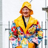 Keiner trotzt dem Regen so schön wie Königin Margrethe. Mit einem gelben Regenhut und passendem Blumen-Regenmantel empfängt sie Graastens Ringreiterverein vor Schloss Graasten.