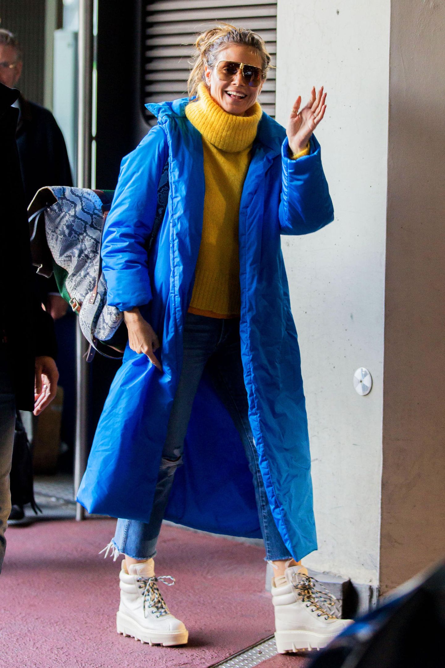 Heidi Klum zeigt sich bei ihrer Ankunft in Berlin nicht nur in bester Laune, sie verbreitet im langen, blauen Mantel von A Plan Application kombiniert mit gelben Woll-Rolli auch welche.