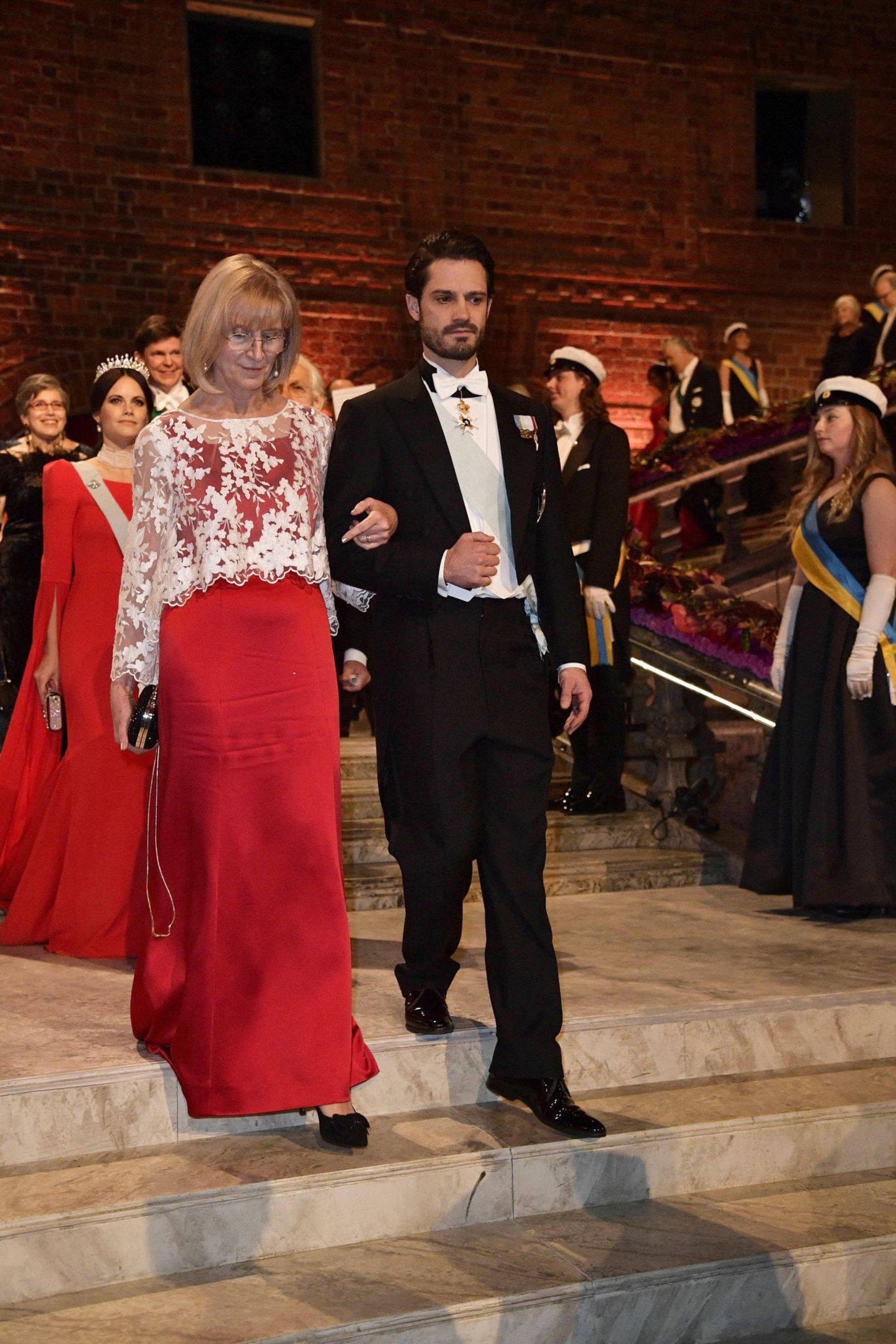 Prinz Carl-Philip tauscht seine Frau (Prinzessin Sofia ist im Hintergrund zu sehen) gegen eine andere "Lady in Red": Er schreitet mit Evi Heldin in Richtung Bankett.
