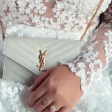 Das Kleid aus dem Düsseldorfer Brautmodengeschäft "IamYours" verzaubert mit durchsichtigen Einsätzen, die von vielen kleinen, weißen Blüten geziert werden. Dazu kombiniert sie eine kleine weiße Tasche von Saint Laurent. 