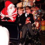 1990  Prinz William und Prinz Harry sitzen neben dem Weihnachtsmann auf einem mit Geschenken vollgepackten Schlitten.