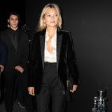 Kate Moss setzt auf einen coolen, schwarzen Zweiteiler unter dem sie eine aufgeknöpfte, weiße Bluse trägt. 