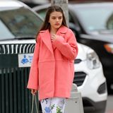 Suri Cruise schlendert in einem coral-farbenen Mantel durch die Straßen New Yorks. Dazu trägt sie eine geblümte Culotte und pinke Puma-Sneaker. In der Hand hält sie lässig eine beige Handtasche. 