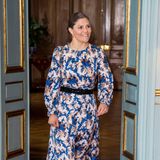 Prinzessin Victoria hat zahlreiche, langarmige Midi-Kleider mit Rundhalsausschnitt im Kleiderschrank. Dieses wild gemusterte Modell kombiniert sie mit schwarzen Accessoires. Gürtel, Handtasche und High Heels sind farblich aufeinander abgestimmt. 