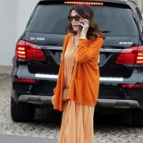 Iris Berben führt ein Telefonat auf der Straße. Sie trägt ein orange-kariertes Blusenkleid mit farblich abgestimmten Cardigan. Beige Accessoires machen den Look perfekt. 