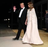 Melania trägt ein bodenlanges Capekleid mit edlen Feder-Applikationen des Labels J.Mendel. Mit knapp 5.000 Euro mal wieder ein echter Luxuslook. Dazu kombiniert die First Lady silberfarbene High-Heels.
