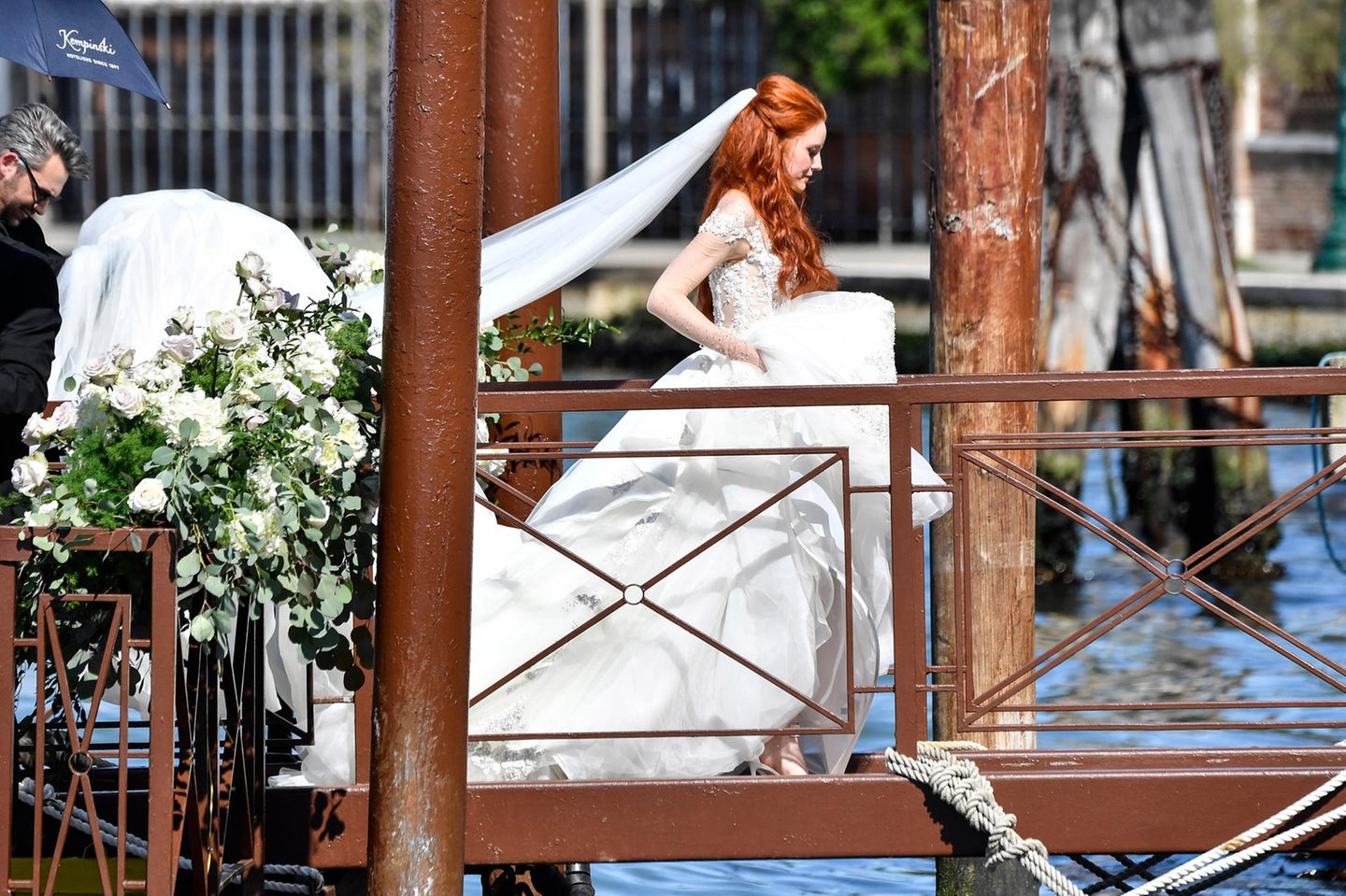 Da kommt die Braut! Wunderschön im floralen Hochzeitskleid mit langer Schleppe und langem Schleier schreitet Barbara Meier auf dem blumengeschmückten Steg Richtung Altar.