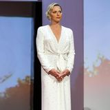 Fürstin Charlène trägt ein bodenlanges, weißes Kleid mit V-Ausschnitt, geraffter Taille und schwarzen, filigranen Punkten. Das Modell stammt aus der Pre Fall Kollektion von Louis Vuitton.