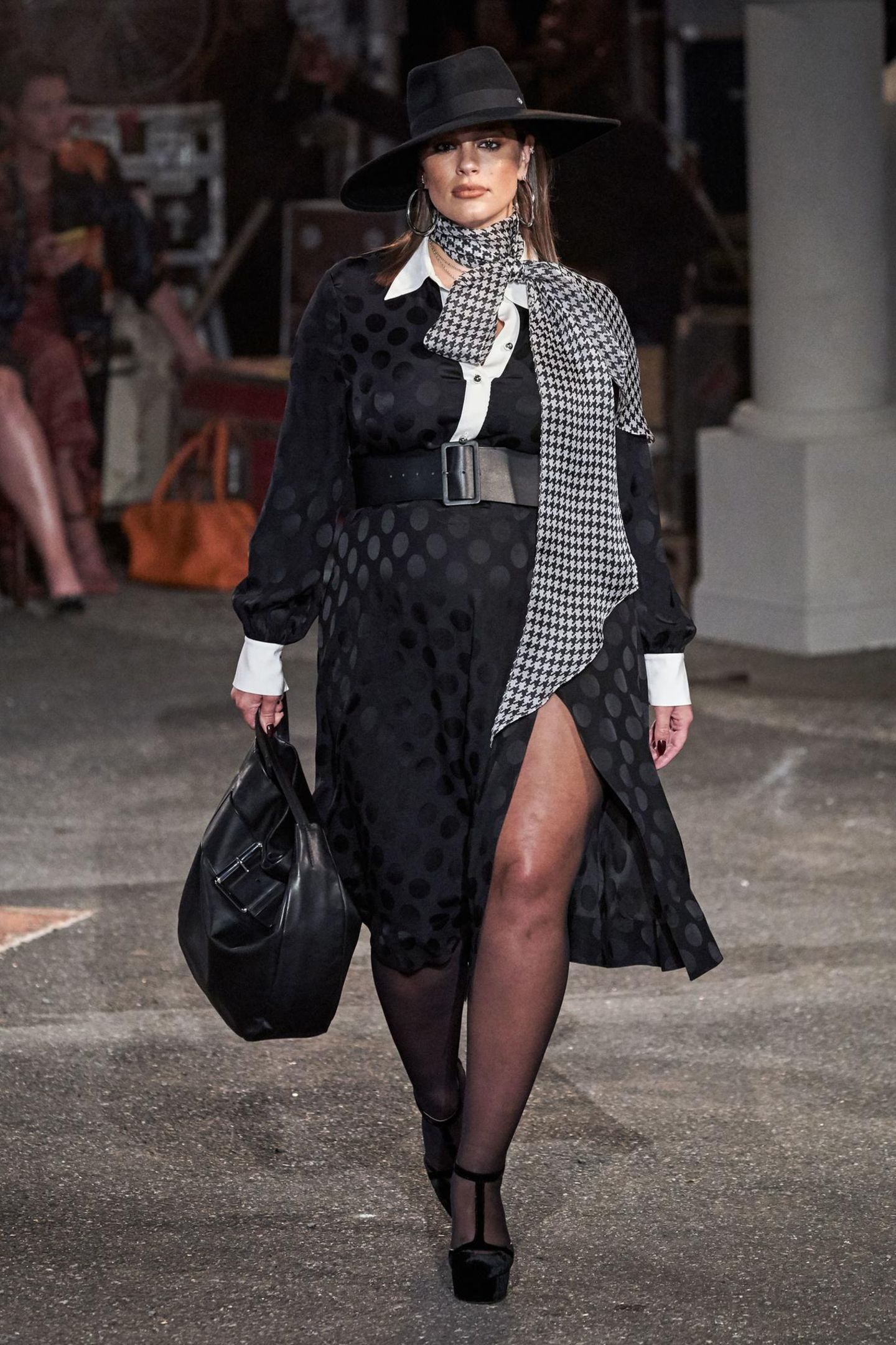 Curvy-Model Ashley Graham läuft in einem schwarzen Maxi-Kleid mit tiefem Beinschlitz und breitem Taillengürtel für den Mode-Guru Tommy Hilfiger über den Laufsteg. 