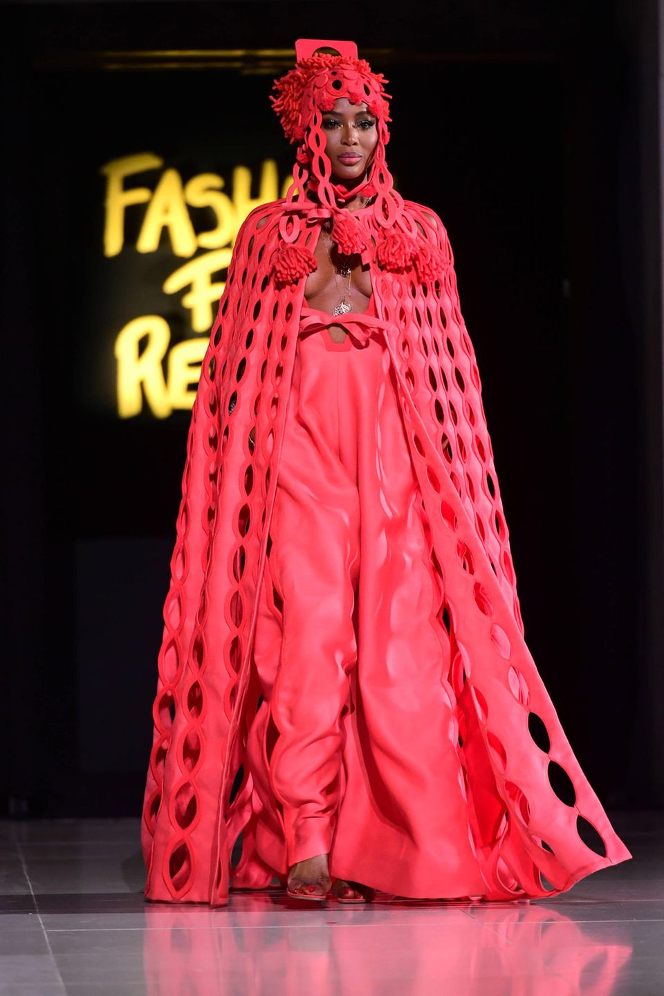 Auch auf dem Catwalk präsentiert Naomi eine extravagante Robe mit Cape und Kopfbedeckung in der Knallfarbe rot – und erneutem Wow-Dekolleté. 